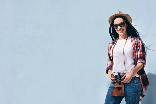 Smiling attractive woman holding camera standing against blue wall