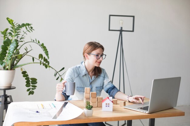 Smiling attractive woman holding coffee cup while working on laptop