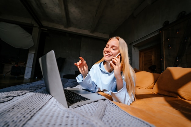 Smiling attractive woman lying on bed talking by smartphone