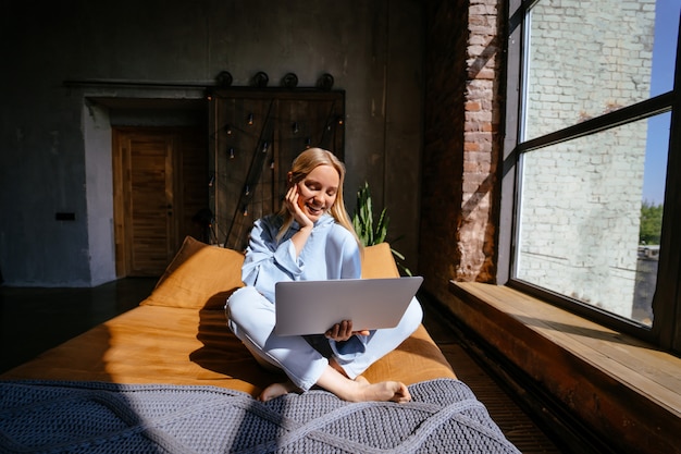 Smiling attractive woman lying on bed using laptop