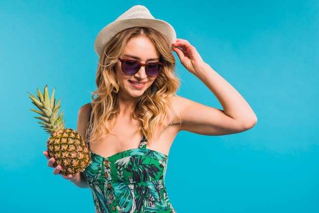 Free photo smiling attractive young woman in hat and sunglasses holding pineapple