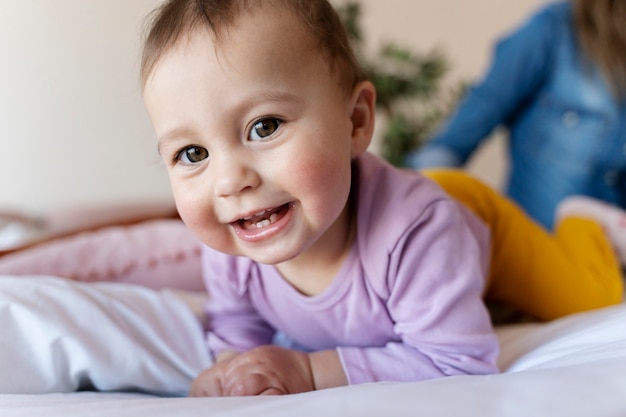 Free Photo smiling baby laying on the bed while his mother is sitting beside him