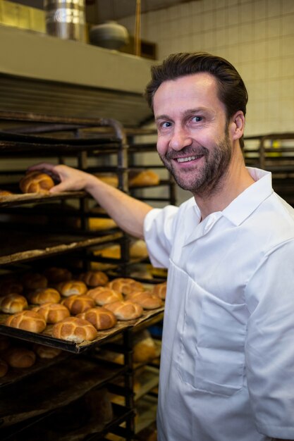 Smiling baker placing baked buns in shelf