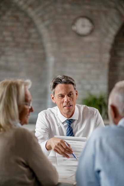 Smiling bank manager showing to his senior customers where to sign on the contract during a meeting in the office