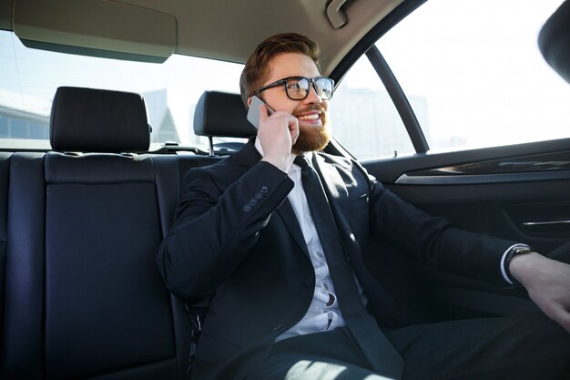 Smiling bearded business man in eyeglasses talking on cell phone