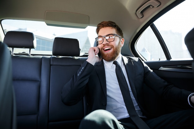 Smiling bearded business man in eyeglasses talking on cell phone