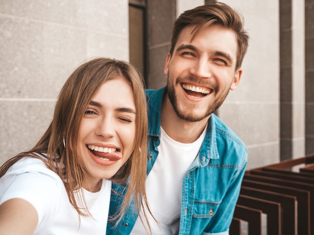 Free photo smiling beautiful girl and her handsome boyfriend in casual summer clothes. happy family taking selfie self portrait of themselves on smartphone camera.having fun on the street. shows tongue