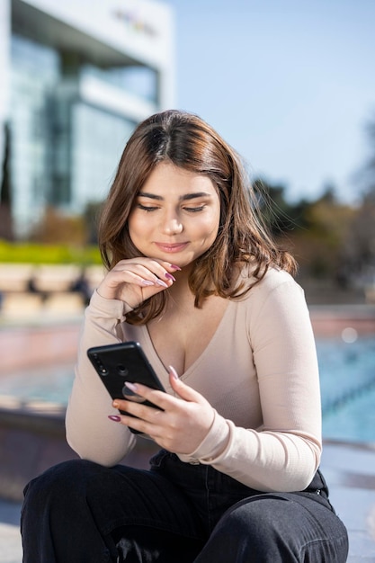 Smiling beautiful girl holding phone and sittin at the park High quality photo