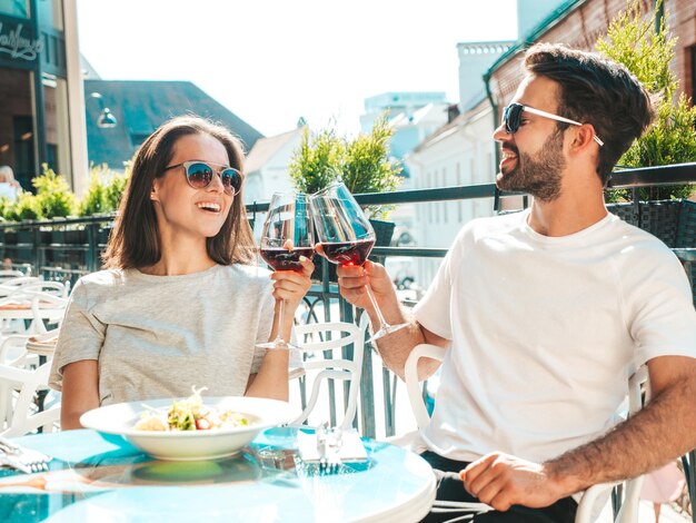 Smiling beautiful woman and her handsome boyfriend Happy cheerful family Couple cheering with glasses of red wine at their date in restaurant They drinking alcohol at veranda cafe in the street