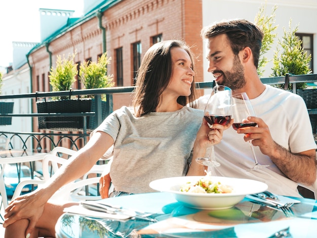 Smiling beautiful woman and her handsome boyfriend Happy cheerful family Couple cheering with glasses of red wine at their date in restaurant They drinking alcohol at veranda cafe in the street