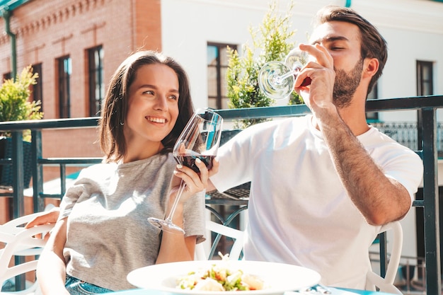 Smiling beautiful woman and her handsome boyfriend Happy cheerful family Couple cheering with glasses of red wine at their date in restaurant They drinking alcohol at veranda cafe in the street