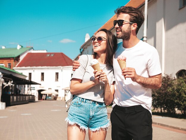 Smiling beautiful woman and her handsome boyfriend Woman in casual summer clothes Happy cheerful family Couple posing on the street background in sunglasses Eating tasty ice cream in waffles cone