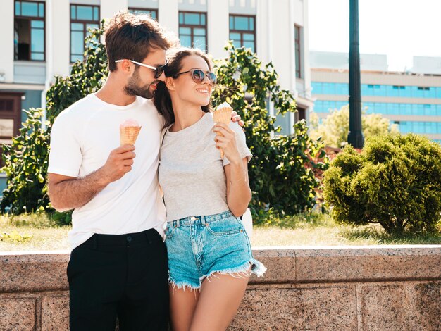 Smiling beautiful woman and her handsome boyfriend Woman in casual summer clothes Happy cheerful family Couple posing on the street background in sunglasses Eating tasty ice cream in waffles cone