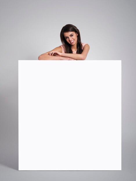 Smiling beautiful woman leaning on empty whiteboard