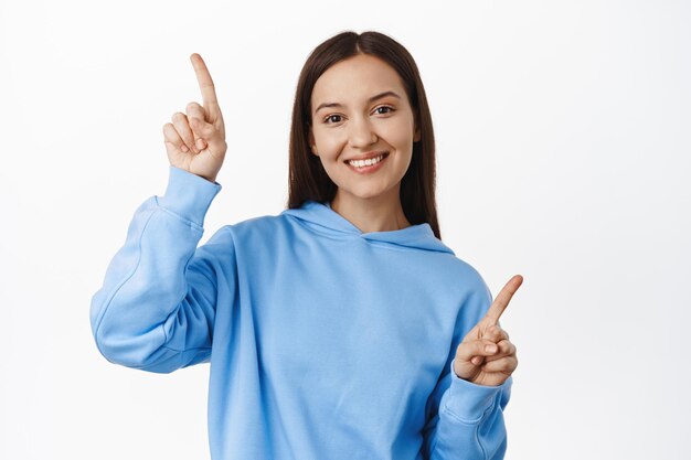 Smiling beautiful woman pointing sideways, showing two choices, variants for customers, standing in casual clothes against white background.