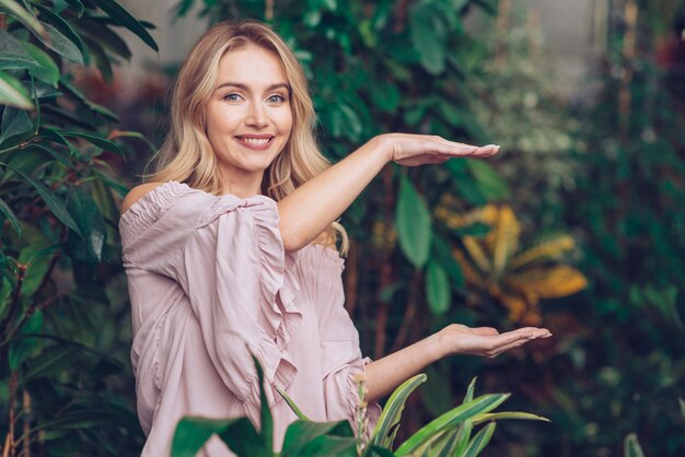 Smiling beautiful young woman showing something on the palms of her hands in the garden