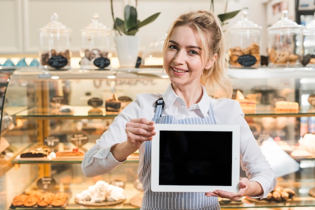 Free photo smiling beautiful young woman standing in front of display cabinet showing blank slate