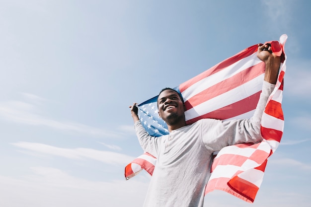 Smiling black man holding waving American flag behind back