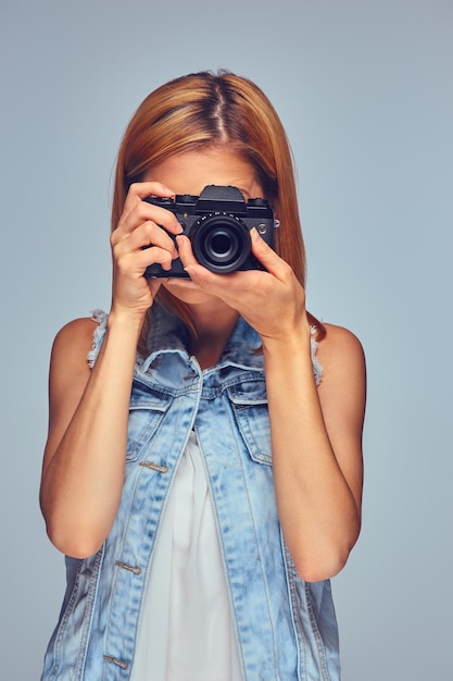 Free photo smiling blond female holds compact digital photo camera, isolated on grey background.