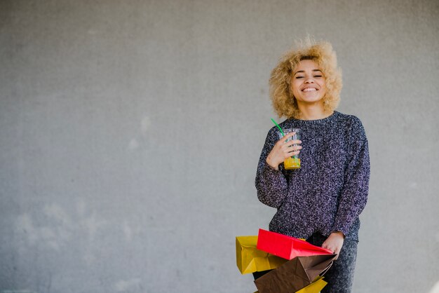 Smiling blond woman with drink and vivid bags