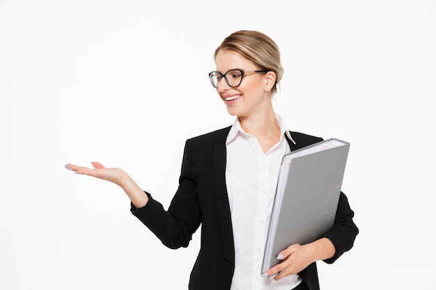 Free photo smiling blonde business woman in eyeglasses with folder in hand holding copyspace on the pound over white wall