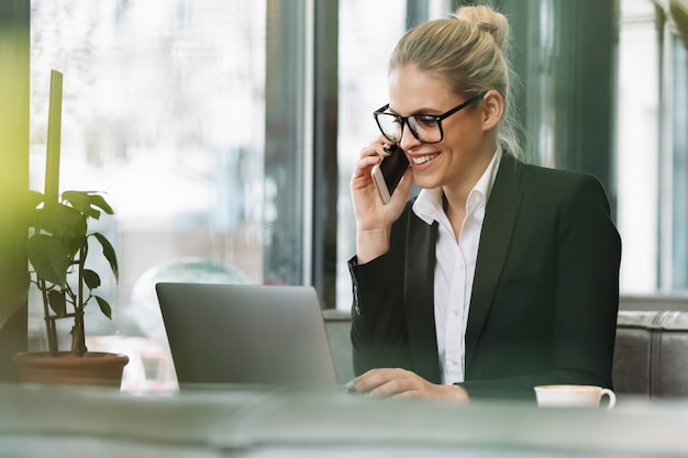 Free photo smiling blonde business woman talking by mobile phone