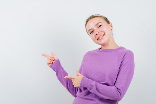 The smiling blonde woman is pointing to left with her forefingesr on white background