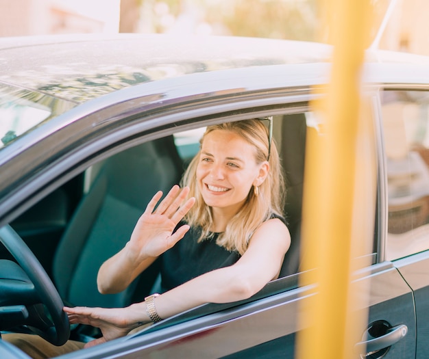 Smiling blonde young woman driving the car waving her hand