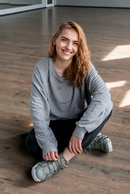 Free Photo smiling blonde young woman sitting on hardwood floor looking at camera