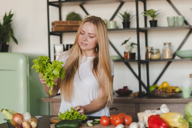 Free photo smiling blonde young woman standing in kitchen sorting lettuce