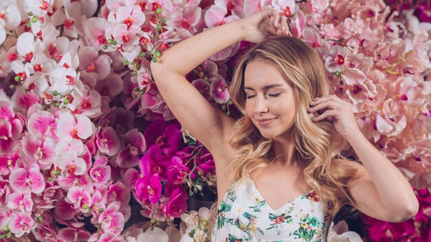 Smiling blonde young woman with eye closed standing against colorful orchids