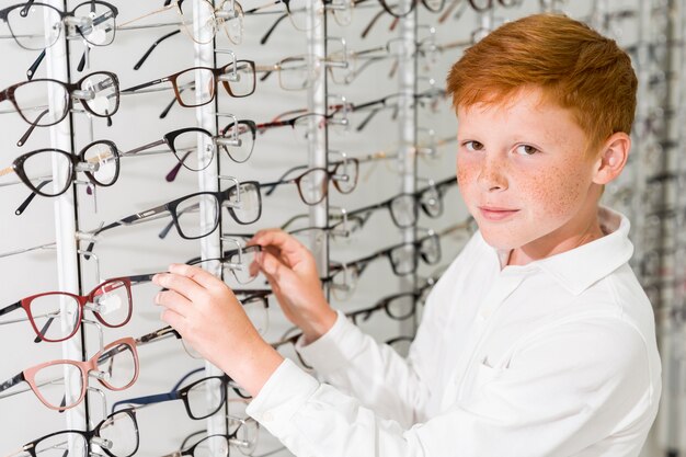 Smiling boy looking at camera while removing eyeglasses front display rack