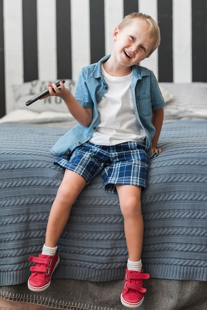 Smiling boy sitting on bed holding smart phone