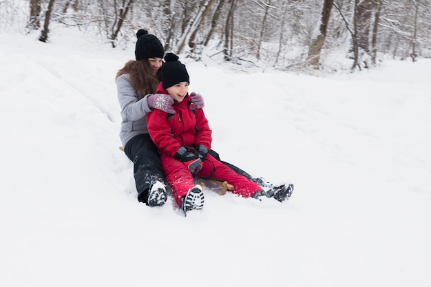 Smiling brother and sister enjoying sledge ride together in winter