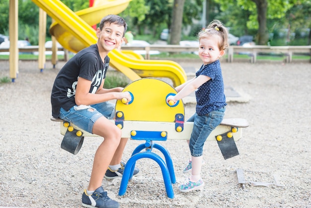 Smiling brother and sister playing seesaw in the playground