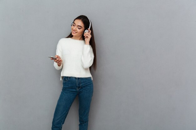 Smiling brunette woman in sweater and headphones listening music