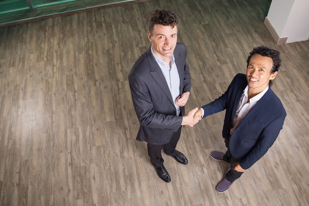 Free photo smiling business men shaking hands in office hall