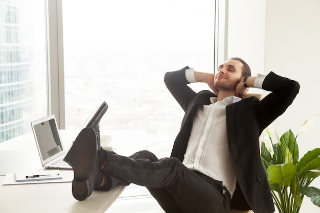 Free photo smiling businessman relaxing at workplace in modern office.