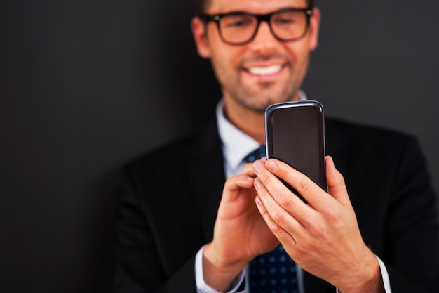 Smiling businessman text messaging on smart phone 
