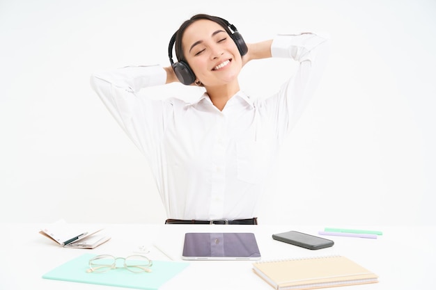 Free Photo smiling businesswoman in headphones sits at office desk listens music and relaxes rests after work w