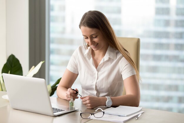 Smiling businesswoman painting nails in office