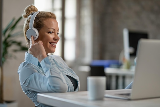 Free Photo smiling businesswoman relaxing with music over headphone while using computer in the office