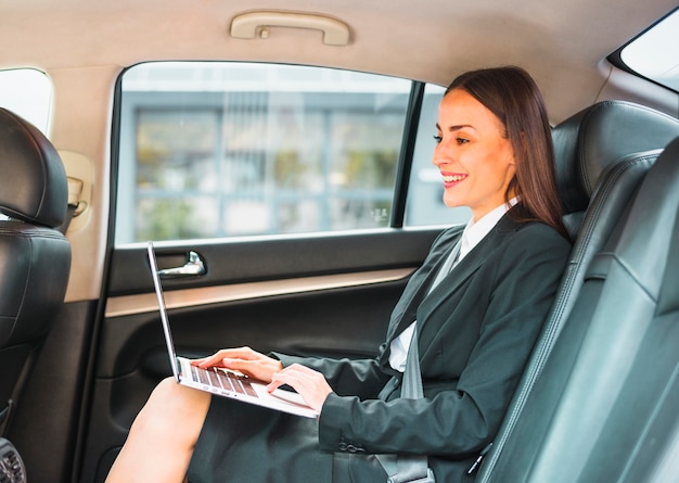 Free photo smiling businesswoman sitting inside car using laptop