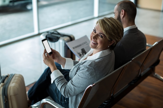 Free photo smiling businesswoman with mobile phone sitting in waiting area