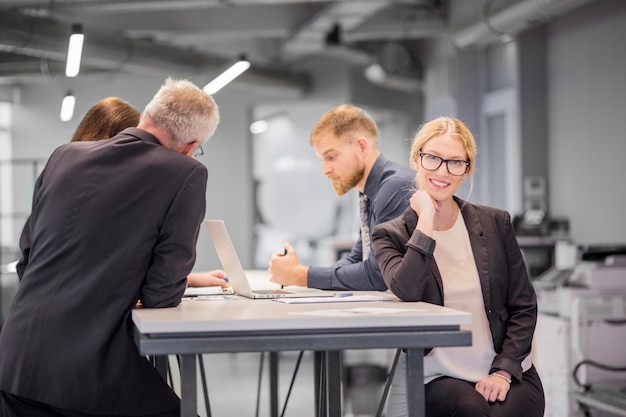 Free photo smiling businesswoman at workplace while her colleague discussing in the office