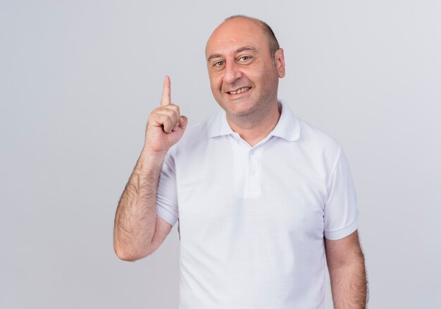 Smiling casual mature businessman looking at camera and pointing up isolated on white background with copy space