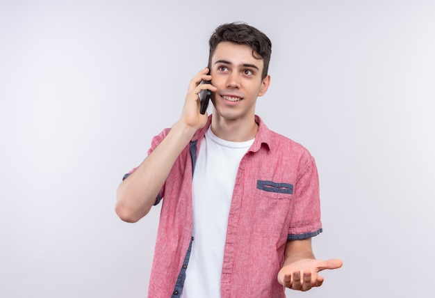 Smiling caucasian young guy wearing pink shirt speaks on phone on isolated white background