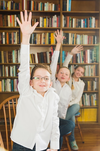 Smiling children putting hands up in library 