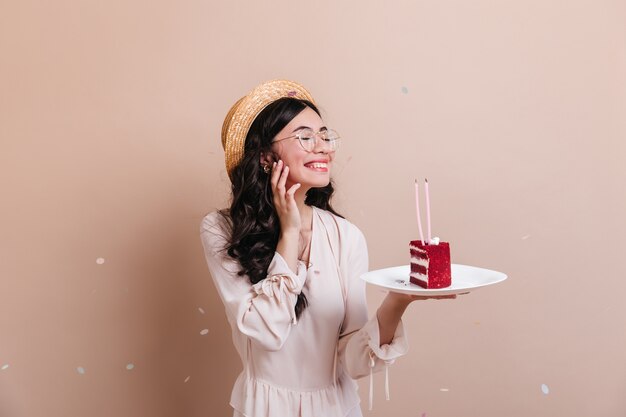 Smiling chinese young woman celebrating birthday. Jocund asian woman holding plate with cake.