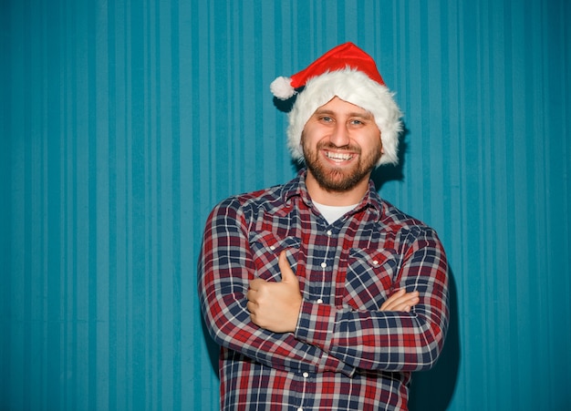 Free photo smiling christmas man wearing a santa hat on the blue studio background